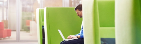 Headerbild: Case Study Bechtle AG, ein Mann sitzt mit Laptop auf grünen Sofas